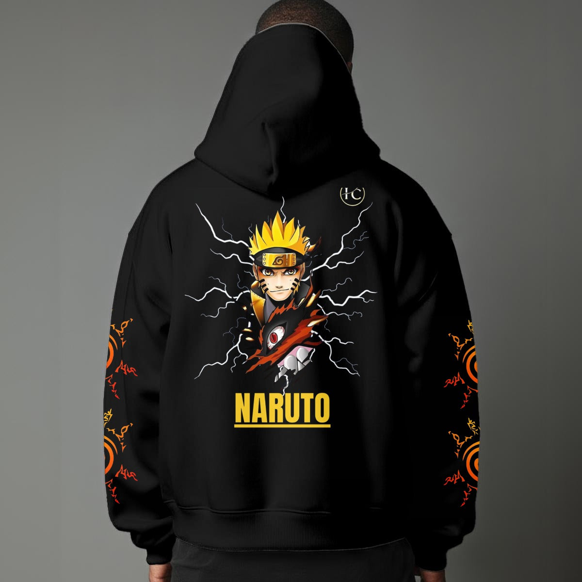Black pullover hoodie featuring Naruto Uzumaki portrait on chest and vertical orange Japanese Kanji text on sleeves, worn by model on grey background.