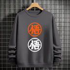 Black crewneck sweatshirt featuring two vertically stacked circular Dragon Ball Z 'Go' Kanji symbols (one orange, one white), flat lay on grey background.