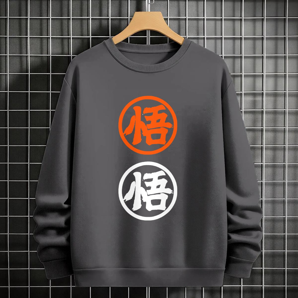 Black crewneck sweatshirt featuring two vertically stacked circular Dragon Ball Z 'Go' Kanji symbols (one orange, one white), flat lay on grey background.