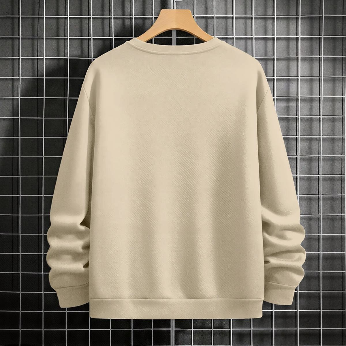 Beige sweatshirt on a wooden hanger against a grid-patterned wall.