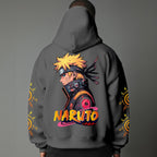 Black pullover hoodie featuring Naruto Uzumaki portrait on chest and vertical orange Japanese Kanji text on sleeves, worn by model on grey background.