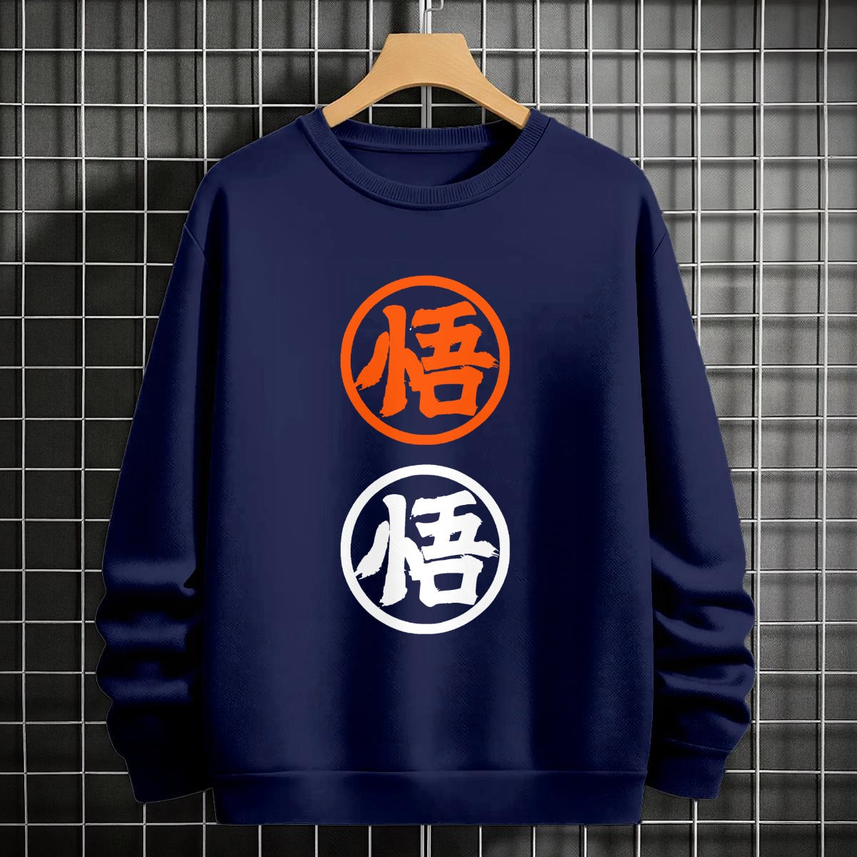 Black crewneck sweatshirt featuring two vertically stacked circular Dragon Ball Z 'Go' Kanji symbols (one orange, one white), flat lay on grey background.